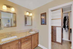 Full bath with double vanity, a walk in closet, and light wood-style floors