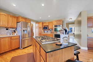 Kitchen featuring a kitchen island, light wood-style floors, stainless steel appliances, a kitchen breakfast bar, and dark stone counters