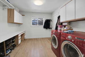 Laundry area featuring cabinet space, light wood finished floors, a desk, and washing machine and clothes dryer