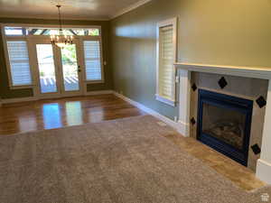 Unfurnished living room with dark carpet, crown molding, a tiled fireplace, and suspended lighting