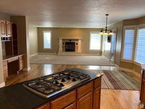 Kitchen featuring stainless steel gas stovetop, light wood finished floors, open floor plan, a textured ceiling, and wood finish cabinets
