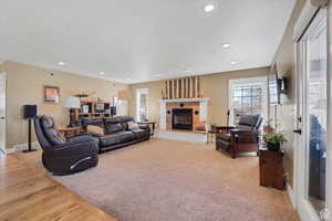 Living area featuring recessed lighting, a fireplace with raised hearth, light carpet, and light wood finished floors