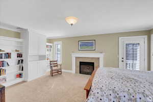 Bedroom with light carpet, a tiled fireplace, ornamental molding, and access to outside