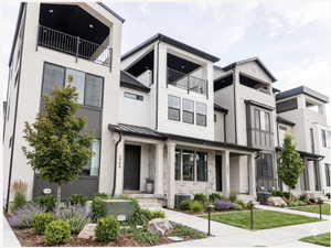 Modern facade featuring multiple balconies, stone accents, contemporary siding, large windows, and manicured landscaping