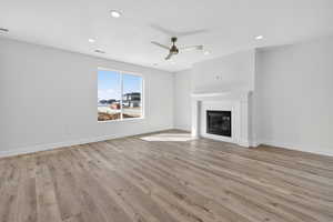 Unfurnished living room featuring a ceiling fan, light wood-style floors, a glass covered fireplace, and recessed lighting