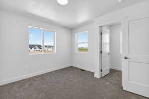 Unfurnished bedroom with dark carpet, a textured ceiling, and multiple windows
