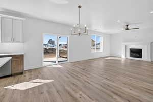 Unfurnished living room featuring ceiling fan, a glass covered fireplace, light wood-type flooring, and suspended lighting