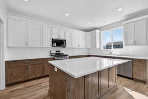 Two tone kitchen with two tone cabinetry, stainless steel appliances, tasteful backsplash, a center island, and light wood-type flooring