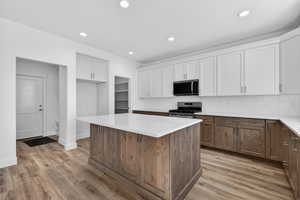 Kitchen featuring stainless steel appliances, two tone cabinetry, a center island, light stone countertops, and decorative backsplash