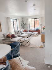 Spacious living area featuring abundant natural light from multiple windows, recessed ceiling lighting, and a neutral carpeted floor