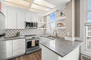 Kitchen featuring a peninsula, open shelves, dark stone counters, stainless steel appliances, and white cabinets