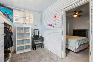 Bedroom with wooden walls, light colored carpet, and a ceiling fan