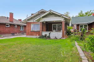 Rear view of property with a lawn, a patio, and brick siding