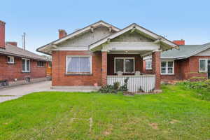 Bungalow with a front lawn, a chimney, a patio, and brick siding