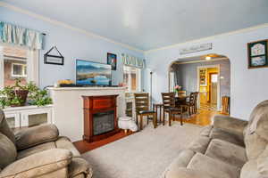 Carpeted living room with arched walkways, crown molding, and a glass covered fireplace