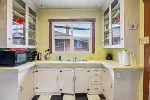 Kitchen with tile counters, glass fronted cabinets, black microwave, and white cabinetry
