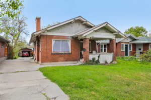 Bungalow-style home featuring a chimney, a front lawn, brick siding, and driveway