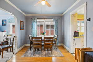 Dining room featuring crown molding, ceiling fan, light wood-type flooring, and arched walkways
