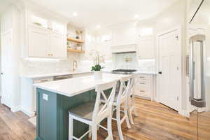 Two tone kitchen with light stone countertops, glass fronted cabinets, a kitchen breakfast bar, light wood-style flooring, and recessed lighting