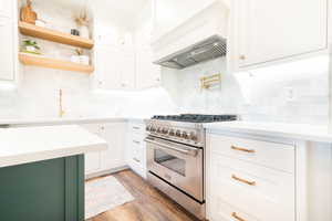 Two tone kitchen with stainless steel range, light stone counters, light wood-style floors, backsplash, and two tone cabinets