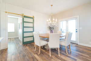 Dining space with a barn door, dark wood-type flooring, and a chandelier