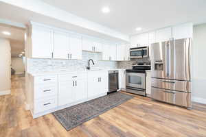 Kitchen with stainless steel appliances, white cabinetry, recessed lighting, light wood-style floors, and tasteful backsplash