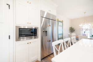 Kitchen with built in appliances, white cabinets, light wood finished floors, a chandelier, and light stone counters