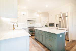 Two tone kitchen featuring two tone cabinets, a center island, high end appliances, light stone countertops, and light wood finished floors