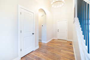 Entryway with arched walkways, suspended lighting, light wood-style floors, and a high ceiling