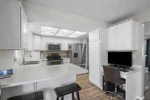 Kitchen with a breakfast bar, a peninsula, stainless steel appliances, light wood finished floors, and white cabinetry