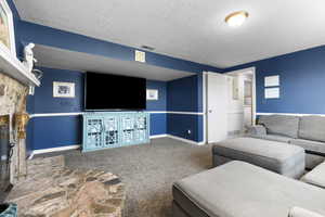 Living area featuring carpet, a textured ceiling, and a stone fireplace
