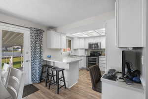 Kitchen with white cabinets, a peninsula, light countertops, stainless steel appliances, and light wood-type flooring
