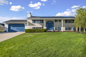 Bi-level home with brick siding, a front yard, solar panels, a garage, and driveway