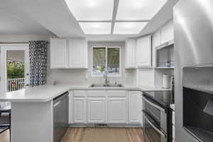 Kitchen featuring a peninsula, stainless steel appliances, a kitchen bar, light countertops, and white cabinetry