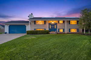 Bi-level home featuring a garage, a yard, solar panels, and driveway