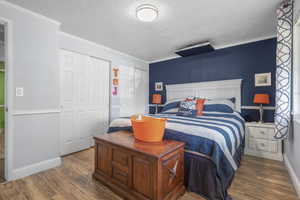 Bedroom featuring multiple closets, wood finished floors, crown molding, and a textured ceiling