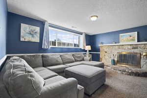 Carpeted living area with a stone fireplace and a textured ceiling