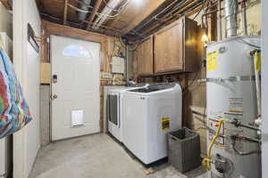 Laundry area with unfinished concrete floors, strapped water heater, washer and clothes dryer, cabinet space, and electric panel