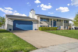 Split foyer home with an attached garage, driveway, a front lawn, brick siding, and roof mounted solar panels