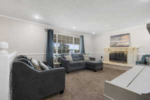 Living room featuring a brick fireplace, dark colored carpet, ornamental molding, and recessed lighting