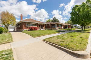 View of front of house featuring brick siding, a chimney, a front lawn, and an outdoor structure