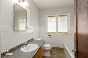 Full bath featuring vanity, tile walls, a tub, and wainscoting