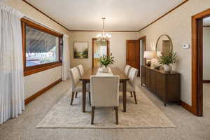 Virtually staged Dining space featuring hanging lights, crown molding, and light colored carpet