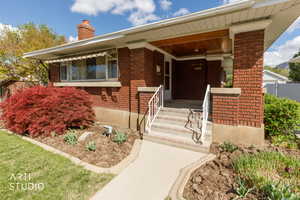 Doorway to property with brick siding, a porch, and a chimney