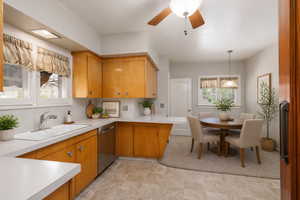 Kitchen featuring light countertops, ceiling fan, dishwasher, hanging light fixtures, and wood finish cabinets