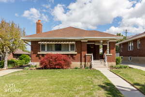 Bungalow-style house with a front lawn, a chimney, covered porch, brick siding, and a shingled roof