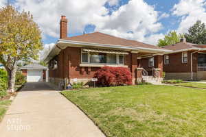 View of front of home with an outbuilding, a chimney, brick siding, a front yard, and a garage