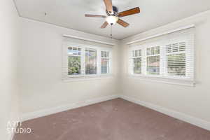 Carpeted empty room with a ceiling fan, healthy amount of natural light, and ornamental molding