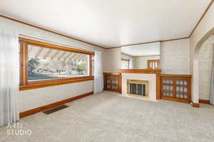 Unfurnished living room with crown molding, light colored carpet, a fireplace, arched walkways, and wallpapered walls