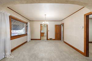 Unfurnished dining area featuring arched walkways, suspended lighting, light colored carpet, a textured ceiling, and ornamental molding